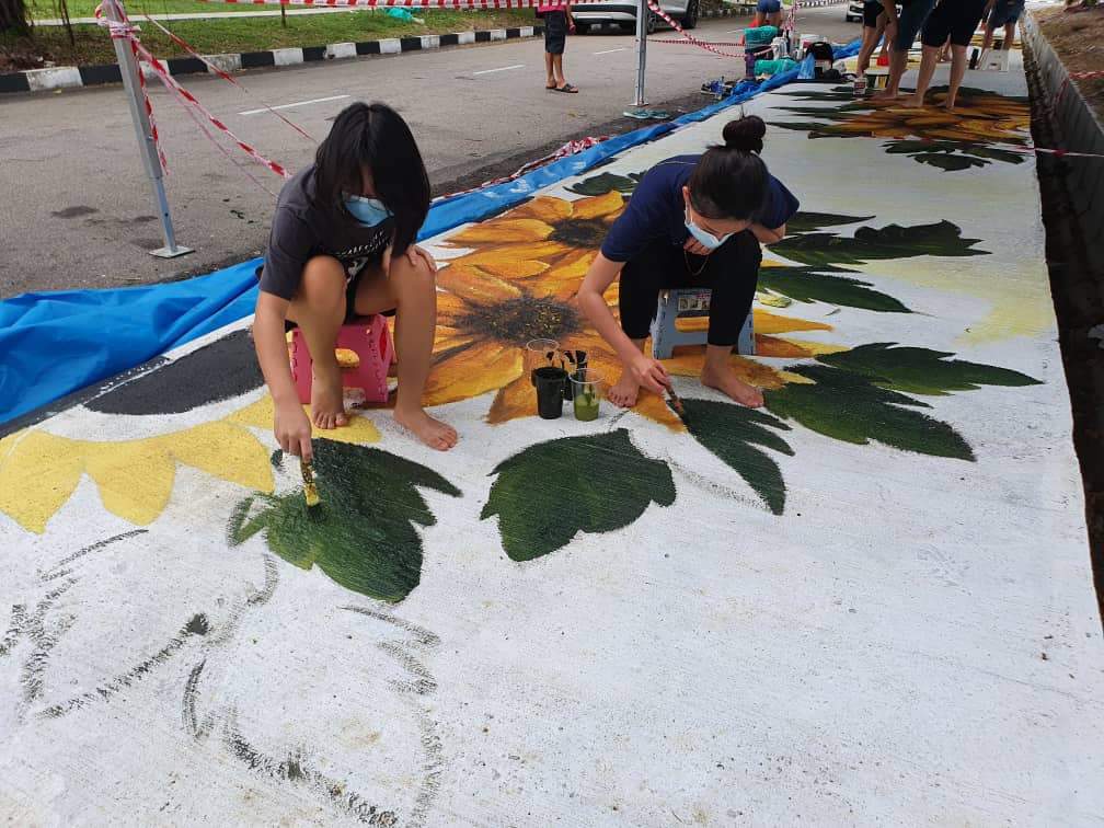 Taman Riang youth volunteers working on a mural of sunflowers on a pathway. – Pic courtesy of by Soon Lip Chee