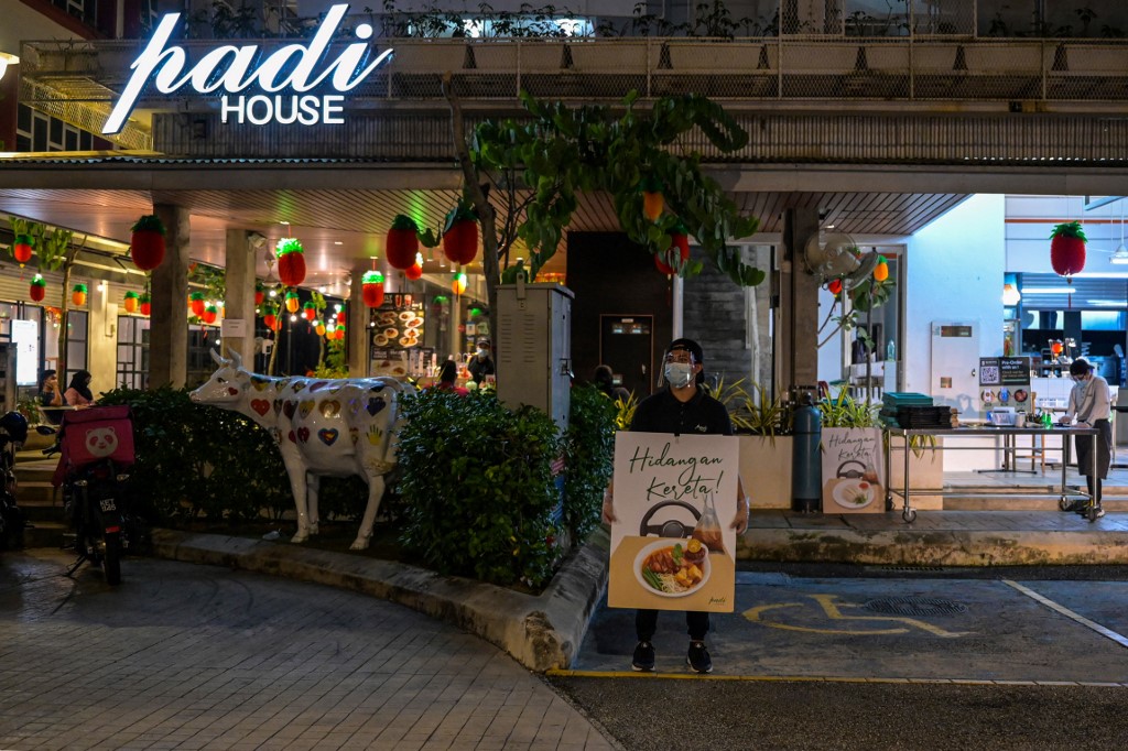 A waiter holding a placard promoting the 'dine-in car' service outside the Padi House restaurant in Cyberjaya. – AFP pic