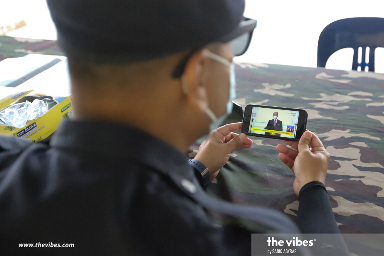 A police officer watching Prime Minister Tan Sri Muhyiddin Yassin's live address session today. Phase 1 of the National Covid-19 Immunisation Programme will include frontliners, such as health workers and defence personnel. – SADIQ ASYRAF/The Vibes pic, February 16, 2021