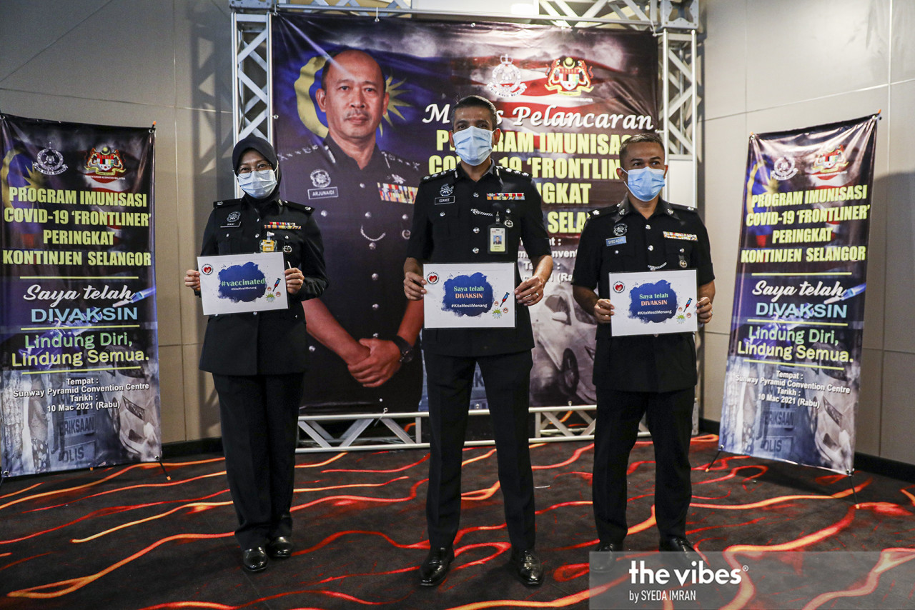 Nik Ezanee Mohd Faisal and two officers holding up posters saying they have been vaccinated. Policemen are included in Phase 1 of the National Covid-19 Immunisation Programme. – SYEDA IMRAN/The Vibes pic, March 10, 2021