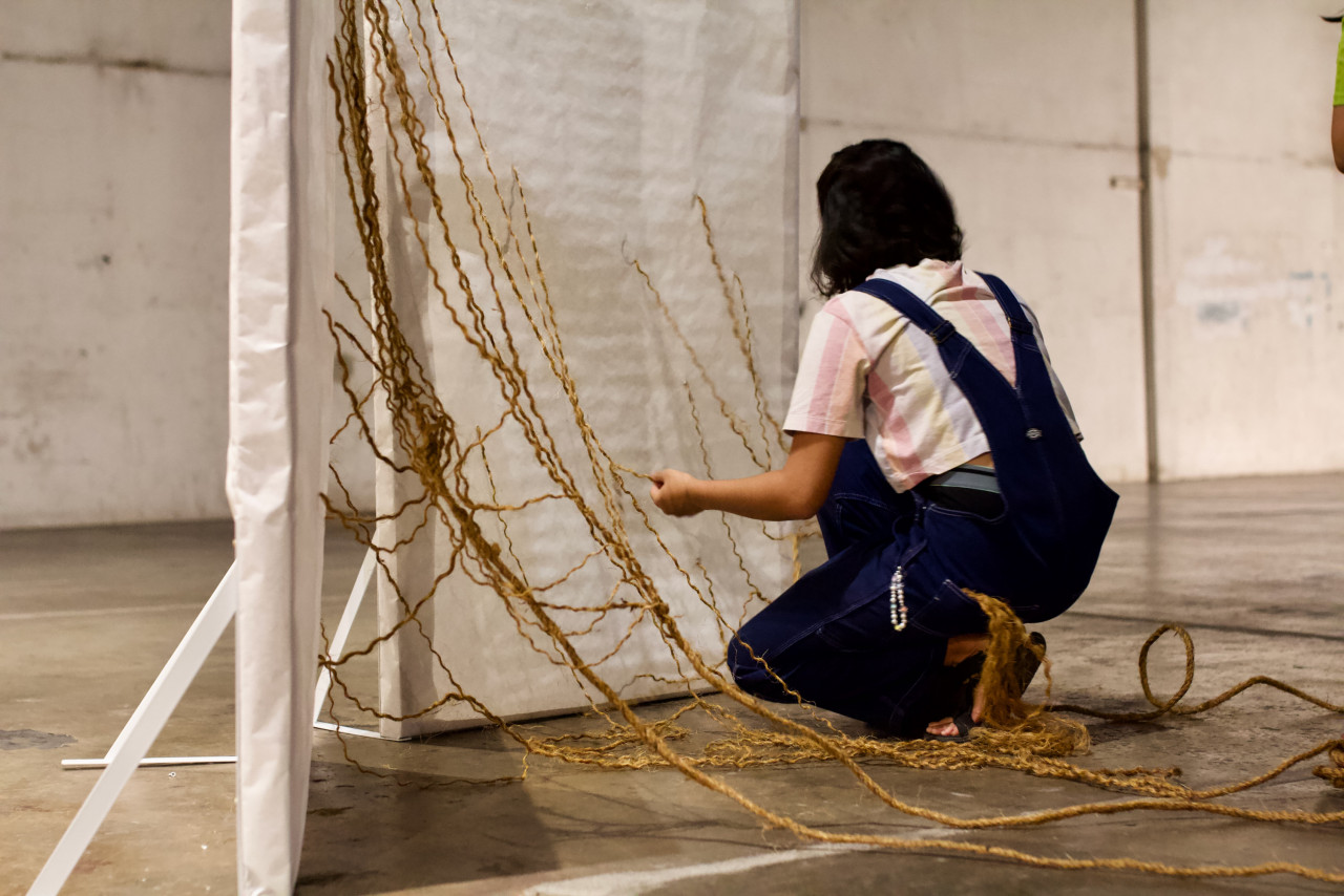 Irynna’s centrepiece provided the set of the staging area. Four ominous ropes, somewhat resembling nooses, dangled down from the high ceiling. On the left side of the stage was a wooden frame screen, covered with white paper and ropes tied through it. After a brief explanation of her piece, she invited five members of the audience to tug at the end of each rope causing it to break apart and collapse to the ground. – Pic courtesy of Nyawa