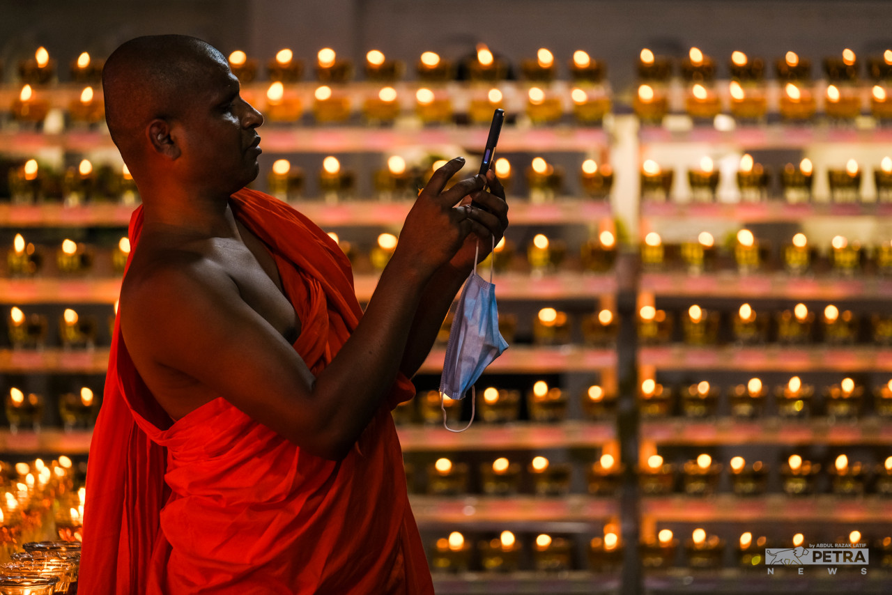 A Buddhist priest taking a photo of the lighted oil lamps. – ABDUL RAZAK LATIF/The Vibes pic