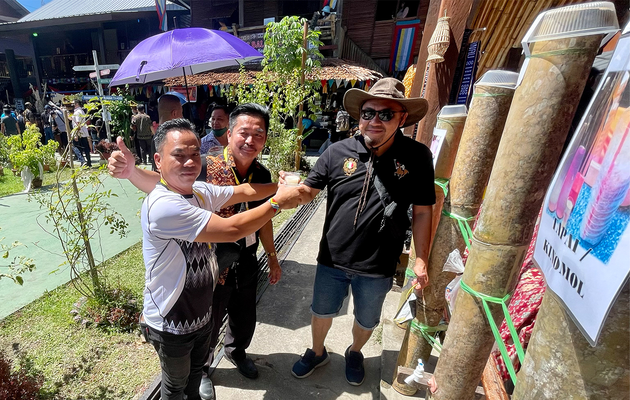 Simon Augustine (right) sharing a drink with new friends at the Ranau Cultural House. – JASON SANTOS/The Vibes pic