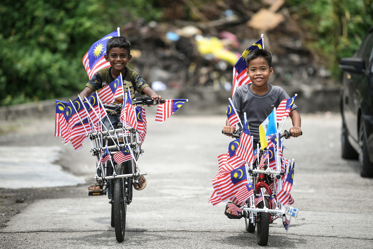 Justin Jacks, 9, (left) and Fikri Asmadi, 12, grinning after Sahul Hamid helped modify and decorate their bicycles with the Jalur Gemilang mini flags in conjunction with the Independence Day celebration. – Bernama pic