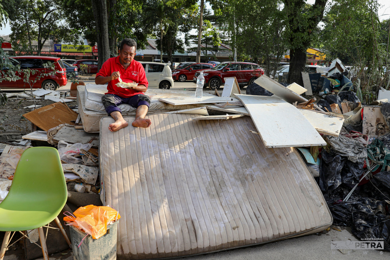 A resident of Taman Sri Muda takes a break to eat, sitting on the remains of items that could not be saved during the recent floods. – AZIM RAHMAN/The Vibes pic, December 29, 2021