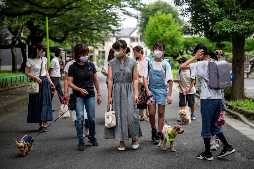Members of the local 'Wan-Wan Patrol', Keiko Shimizu (front left) with her Yorkshire Terrier (below left), Marika Igarashi (centre) and 12-year-old Yurika Igarashi (second from right) with three-year-old poodle Sakura (below right) as they walk along a street to an elementary school in Tokyo on July 14. – AFP pic