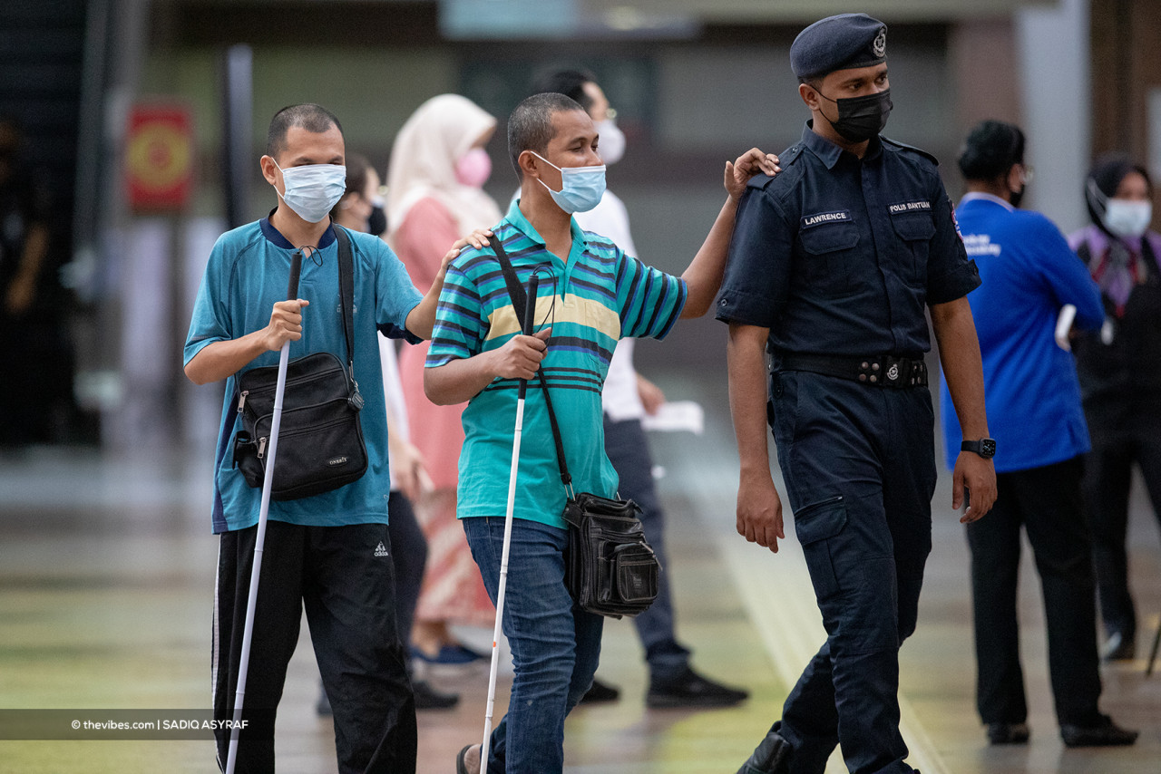 A policeman helps two OKU navigate a vaccination centre, an example of how we need to help one another great through this time of crisis. – SADIQ ASYRAF/ The Vibes pic