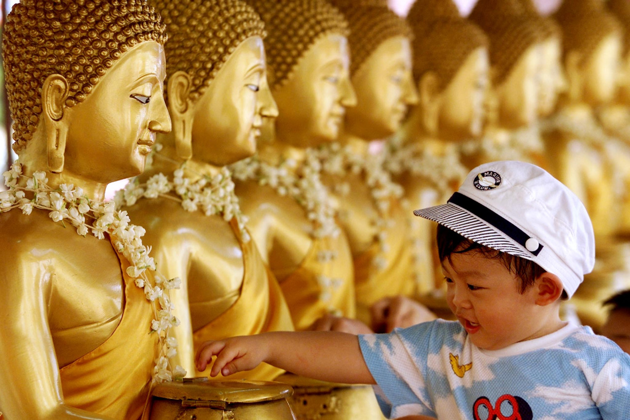 A little girl drops coins into golden Buddha statues as a symbol of blessing at a Buddhist temple in Kuala Lumpur on Wesak Day May 7, 2001. – AFP pic