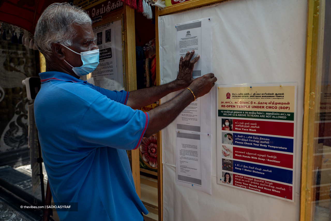 A temple official puts up notices on the Covid-19 standard operating procedures that must be complied with by those who wish to enter a house of worship. – SADIQ ASYRAF/The Vibes pic, November 4, 2021