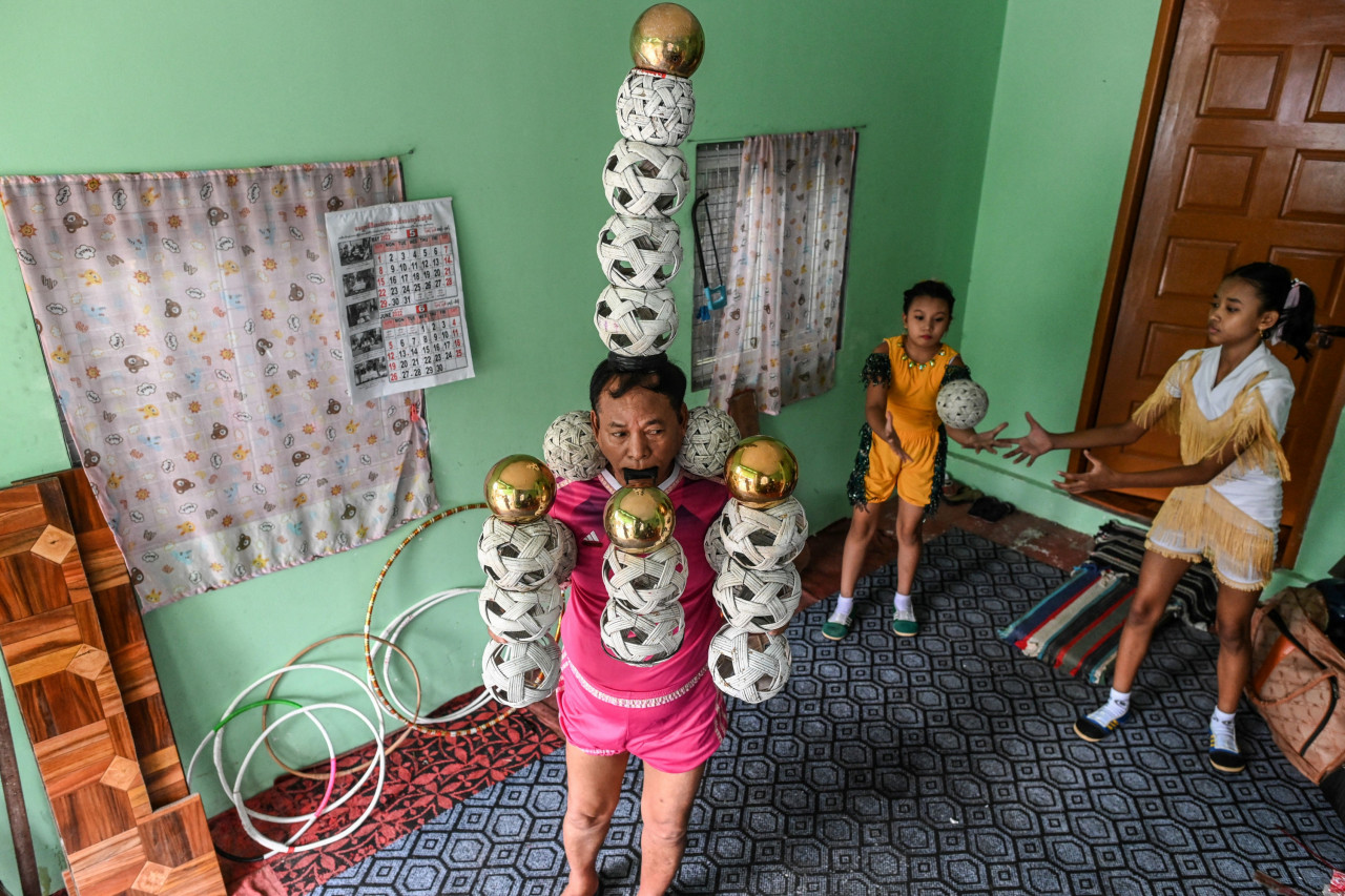 This photo taken on July 5, shows septuagenarian Ohn Myint (front) balancing balls as his granddaughter Han Myint Mo (background R) reacts during a juggling training session. – AFP pic 