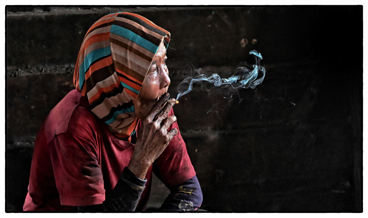 An older woman enjoys a cigarette at a charcoal factory in Kuala Sepetang. – Pic courtesy of Philippe Durant