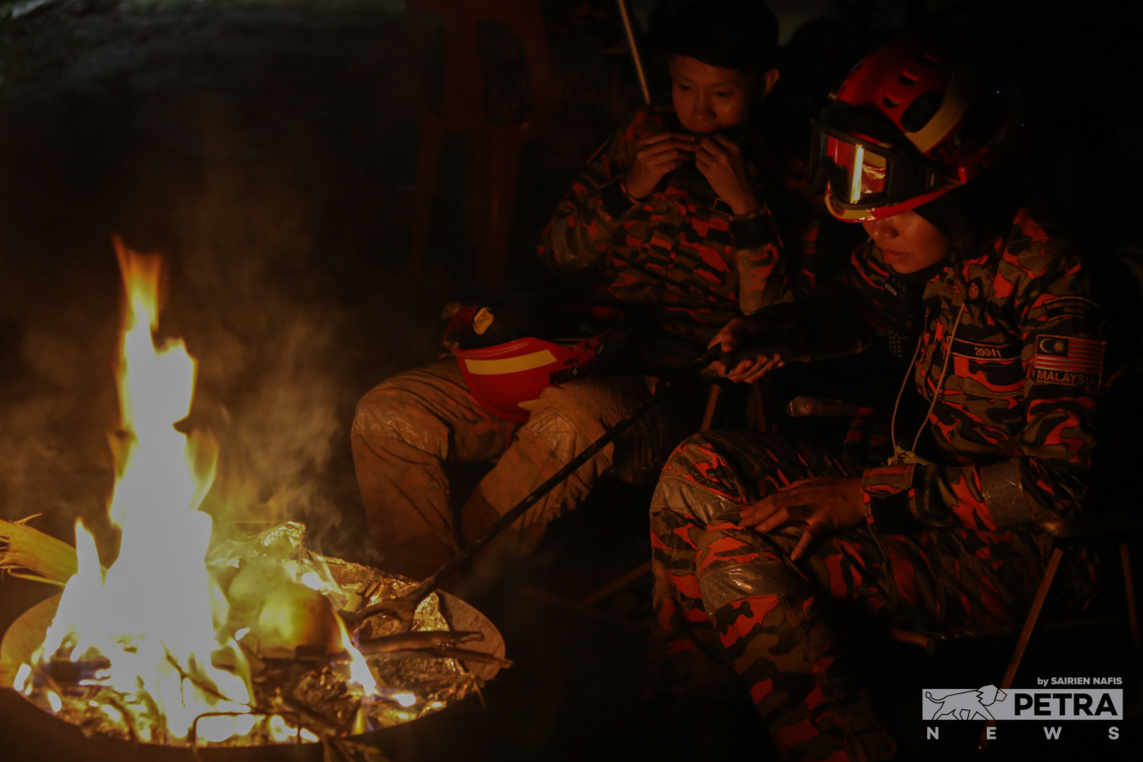 Rescuers in Batang Kali gather around a fire for warmth on the fifth day of the search, last night. – SAIRIEN NAFIS/The Vibes pic, December 21, 2022