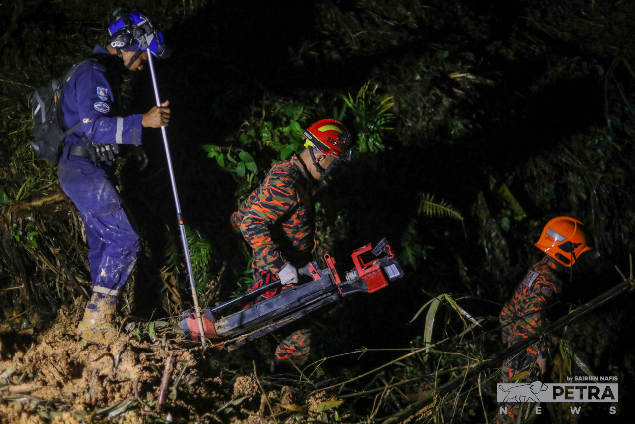 A Fire and Rescue officer carries a searchlight as he is joined by other rescuers, including a SMART officer (blue uniform) to resume the search for the last landslide victim at about 8pm, after temporarily halting at about 5pm. – SAIRIEN NAFIS/The Vibes pic, December 25, 2022