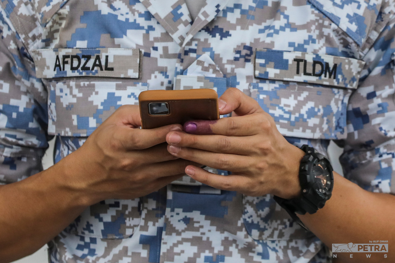 An officer from the Royal Malaysian Navy checks his phone after the early voting process, with his finger dipped in indelible ink to signal that he has done his duties as a rakyat for the 15th general election at SMK Pangkalan TLDM in Lumut today. – ALIF OMAR/The Vibes pic, November 15, 2022 
