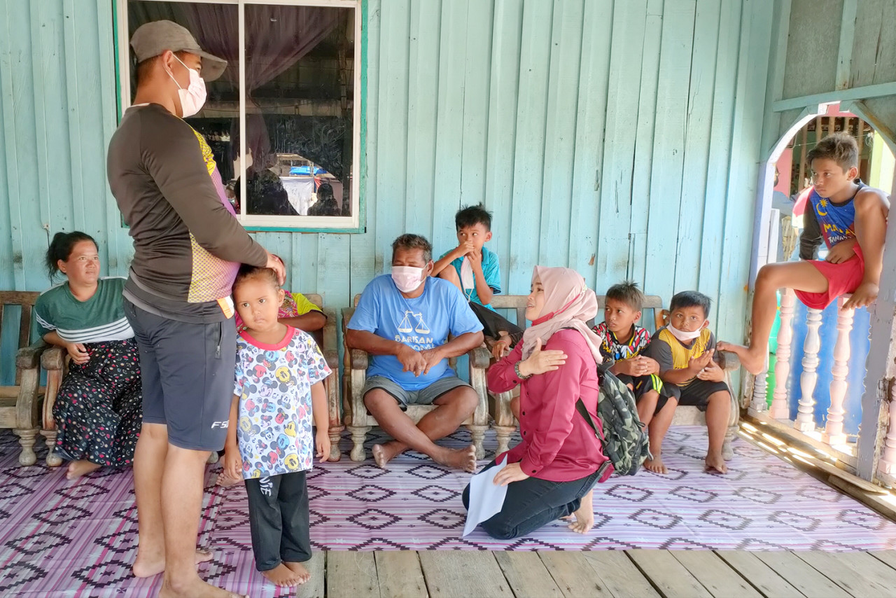 Sekong community development leader Hazulizah Mohd Dani (kneeling) speaking to residents when going door to door in Kg Upak, where previously, no one had registered for the Covid-19 vaccine. – The Vibes pic, June 20, 2021