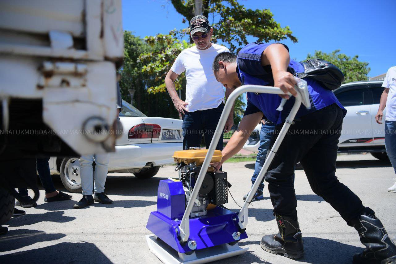 Sepanggar MP Datuk Mohd Azis Jamman (white T-shirt) looks at the compact machine he had purchased to tar and fill potholes in his constituency. – Mohd Azis Bin Jamman Facebook pic, September 14, 2022