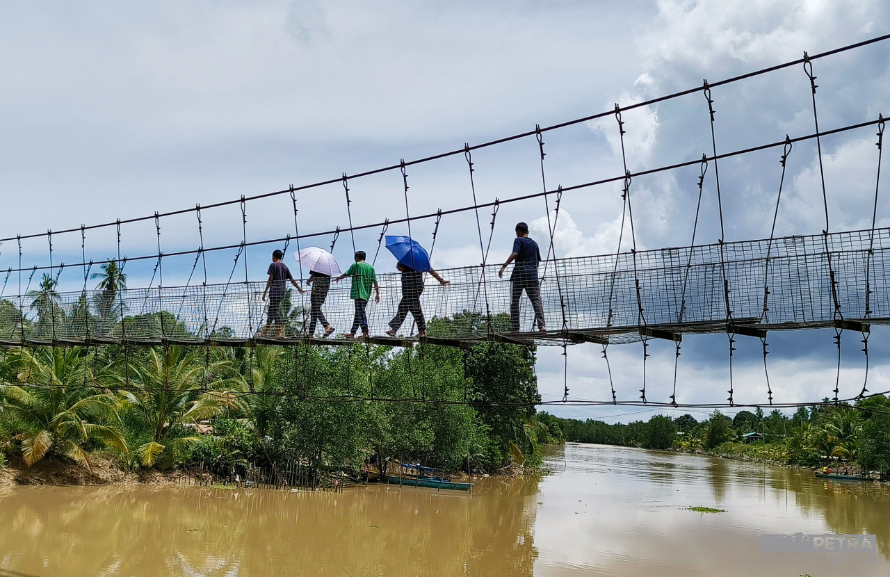 Secondary school boys crossing the dilapidated hanging bridge from Kg Nelayan Tengah to the mosque in Kg Sibugal Besar for Friday prayers. – REBECCA CHONG/The Vibes pic, October 4, 2022