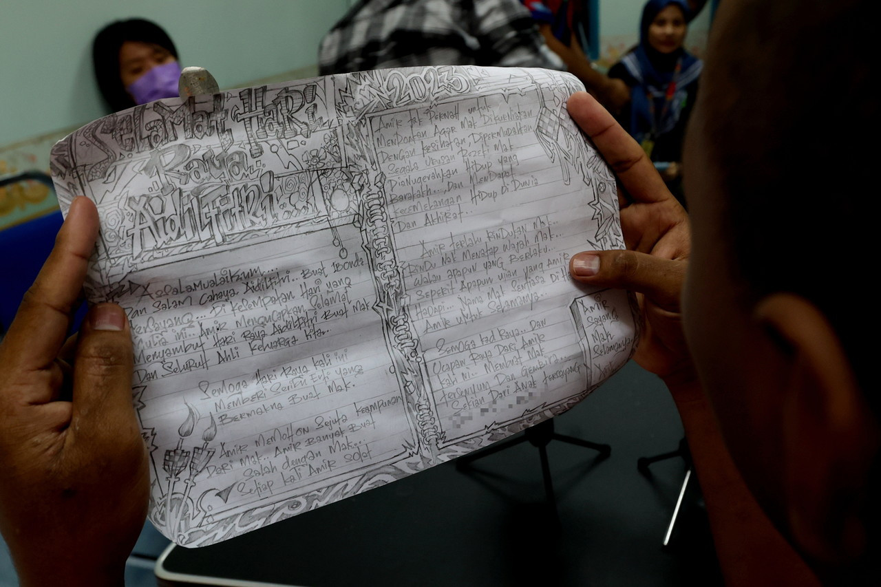 A woman holds up a letter written from prison by her son. This year, she will finally get to celebrate Aidilfitri with her beloved Amir. – The Vibes, April 20, 2023  