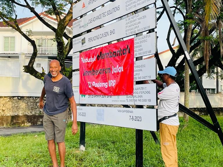 Save Padang member Munis Muniandy (pic) shows a bunting that has been put up on a signboard for the access road project as a protest. – Pic courtesy of Save Padang BRP, May 11, 2023