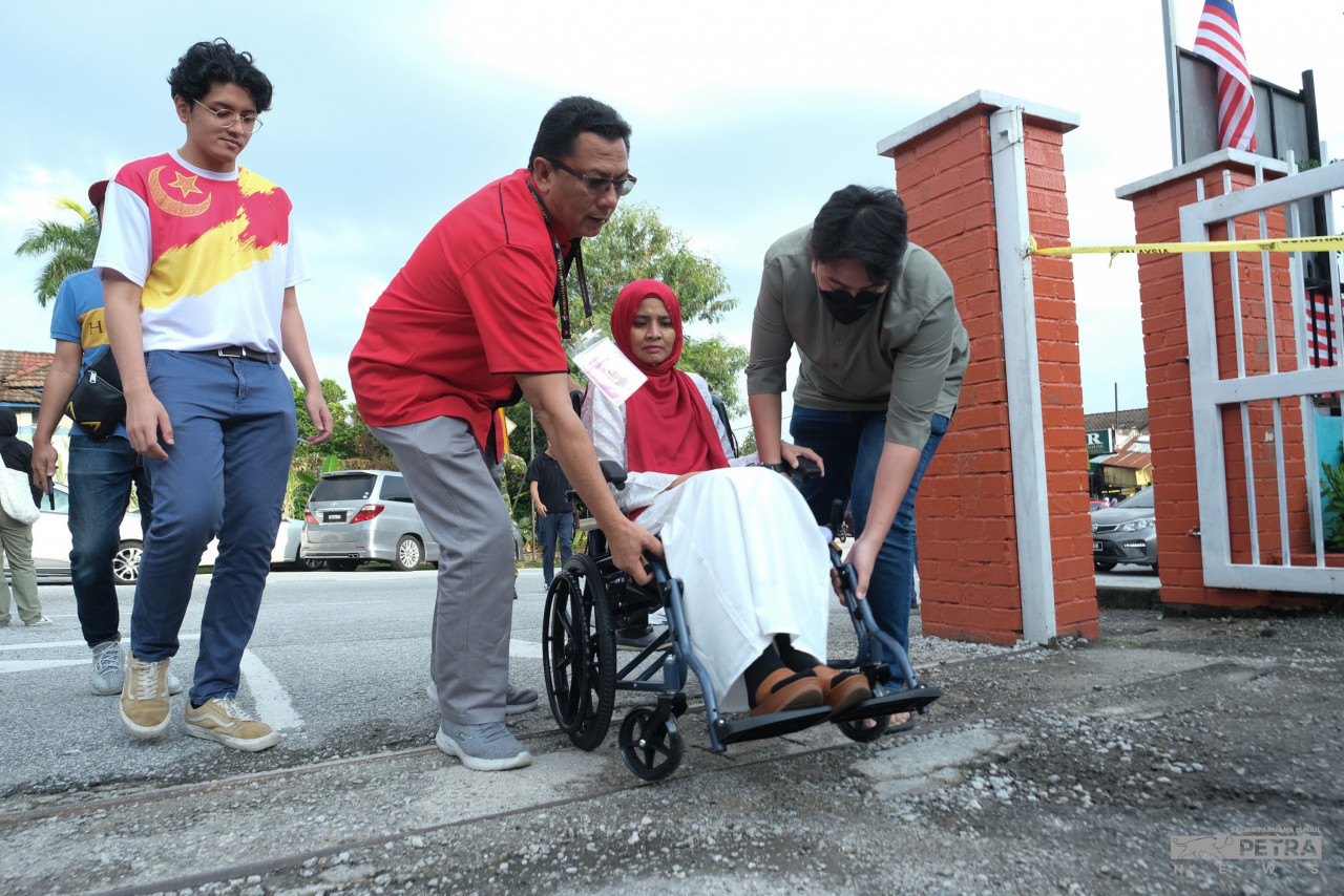 Pakatan Harapan’s candidate for Bukit Antarabangsa, Kamri Kamaruddin, helps his wife enter the polling centre. – SALWA FARHANA ISMAIL/The Vibes pic, August 12, 2023