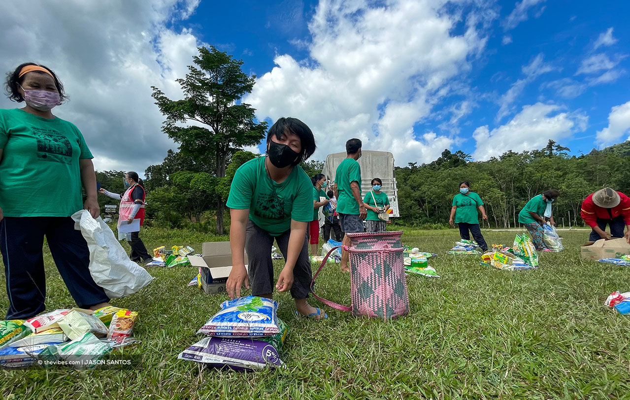 A woman picks up a bag of rice to put in her traditional bag, called ‘saging’ , while her friend looks on. – The Vibes pic, July 17, 2021