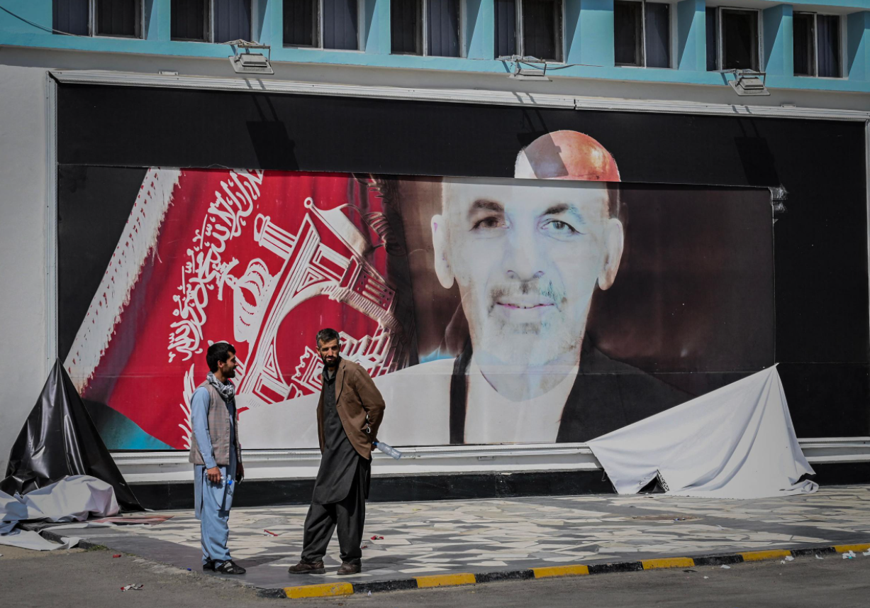Two men talking at an airport in the Afghan capital Kabul with a torn poster of exiled leader Ashraf Ghani behind them. – AFP pic, August 22, 2021