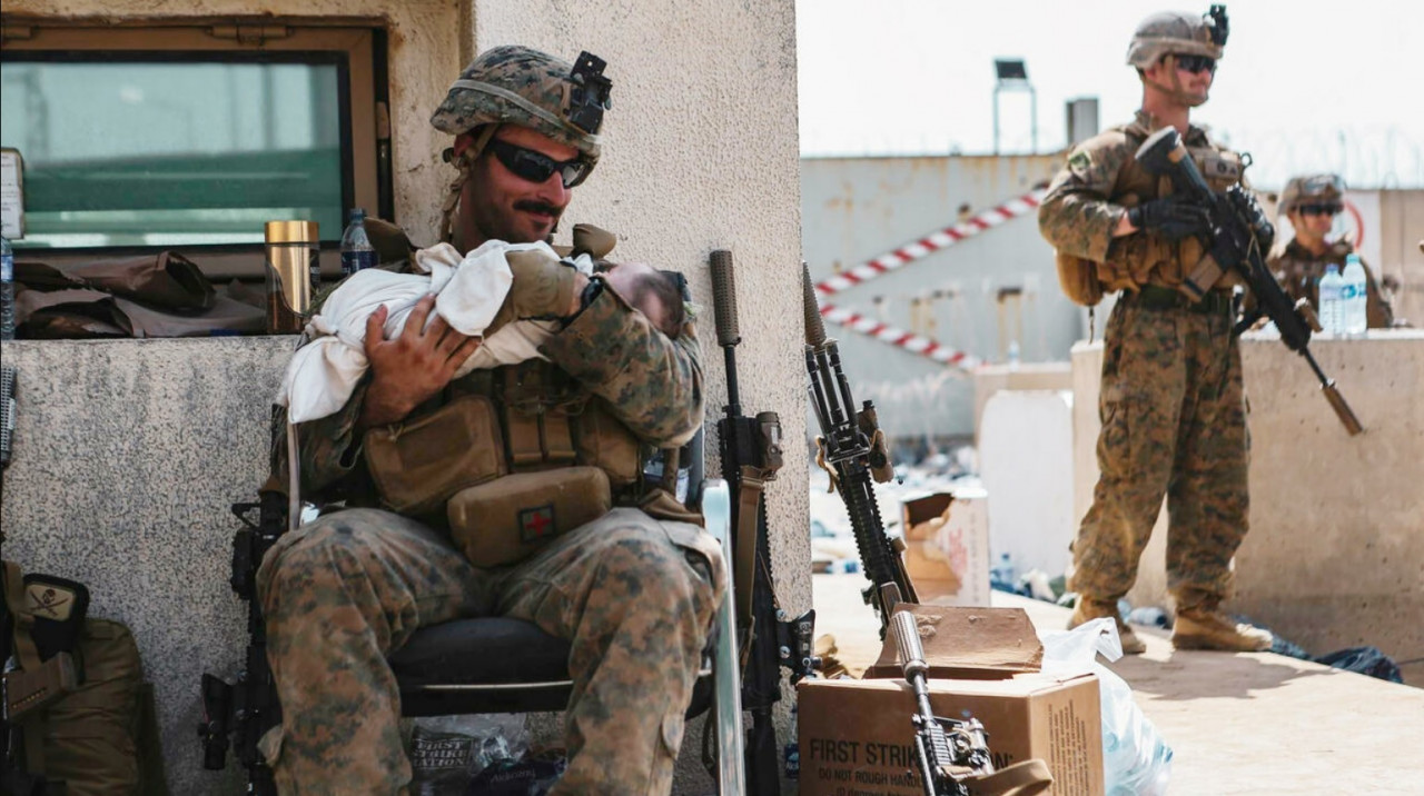 A soldier in his combat gear sits with a blanketed baby in his arms. – AFP pic, August 21, 2021